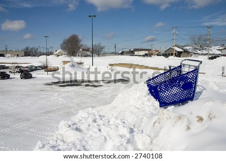 Shopping cart at the top of tall snow bank in a parking lot.