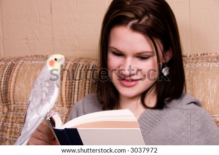Attractive teen reading on the couch with a bird perched on the book.