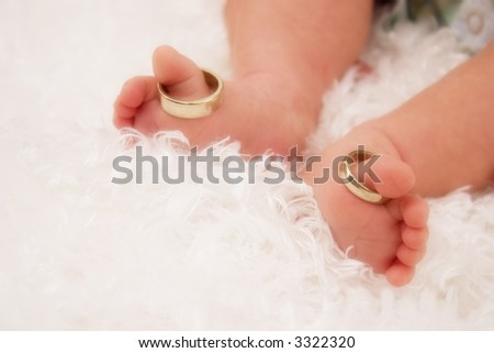Feet of a newborn wearing his parents' wedding rings on his big toes.