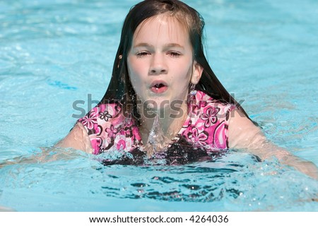 Preteen girl coming out of the pool water for a breath of air.