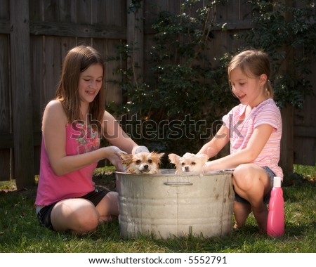 Two girls washing two Pomeranian puppies outside in an old tin tub.