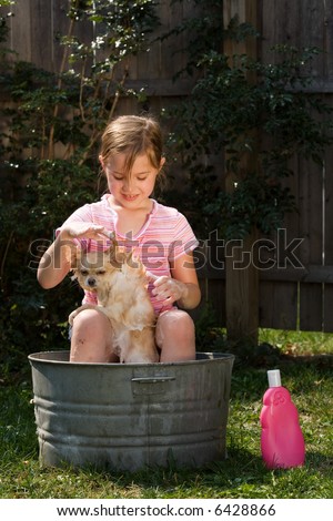 A cute little girl outside washing her Pomeranian puppy in an old, tin tub.