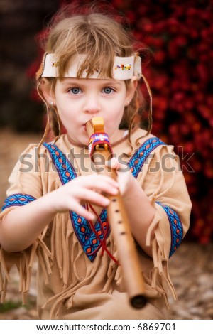 Cute blond girl in native American attire playing a wooden flute.