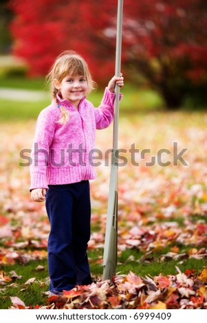 Young elementary girl pausing by a pile of leaves she\'s just raked.