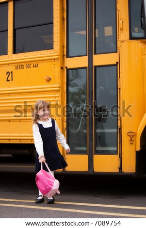 Little girl standing by a big school bus door with her pink backpack.