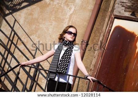 Pretty preteen standing on a fire escape on a sunny day.