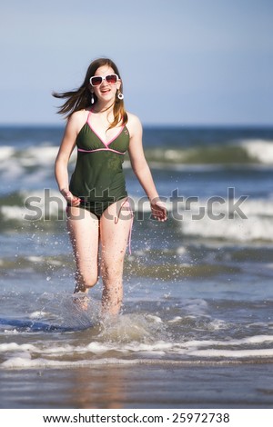 A preteen girl running out of the ocean surf.