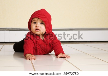 A biracial baby girl looking up as she tries to creep across a white, tile floor.