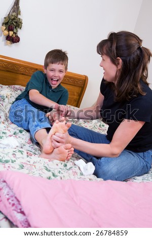 A mother tickling her son\'s feet on a big bed.
