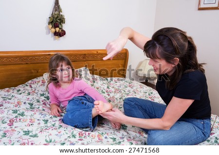 A mom bringing her tickling finger towards the barefoot of her elementary daughter.