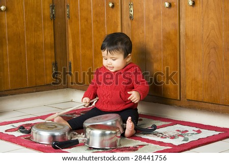 A cute baby girl drumming on pots and pans with a wooden spoon.  Spoon with some motion blur. - stock photo