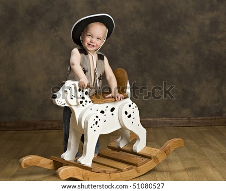 Adorable little boy in a cowboy hat and vest riding a rocking dog.