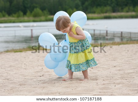 Curious little girl walking with balloons along the beach