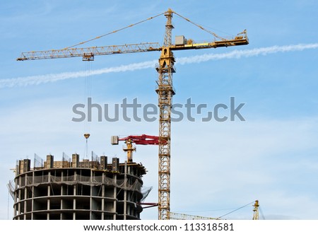 Tower crane and reinforced building under construction; project site against blue sky