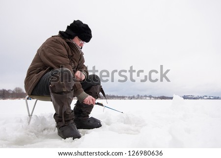Russian fisherman in earflapped fur hat and boots at winter fishing