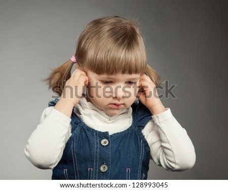 Little girl covers her ears, grey background