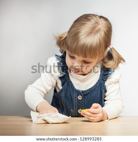 Little girl puts things in order with duster in her room, grey background