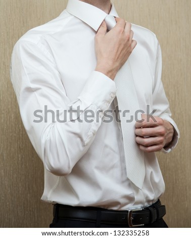 Young man in white shirt straightenes his tie