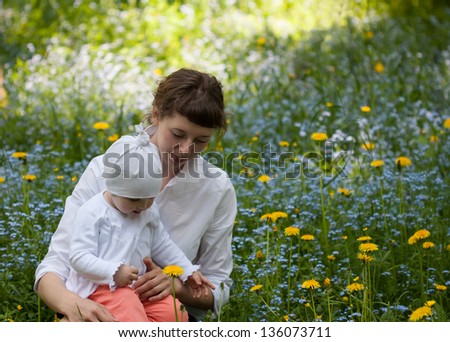 Little baby girl with her mother among foget-me-nots and dandelions