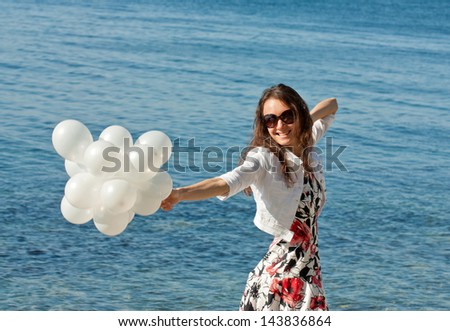 Happy smiling young woman playing with white balloons at the sea