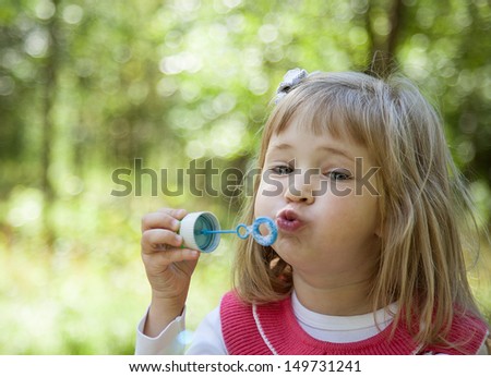 Charming little girl making soap bubbles in a summer park