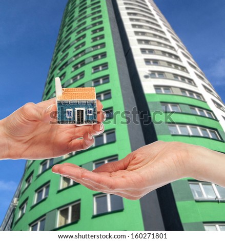 Concept of buying a house - hand giving small house model to the other hand, modern building in the background