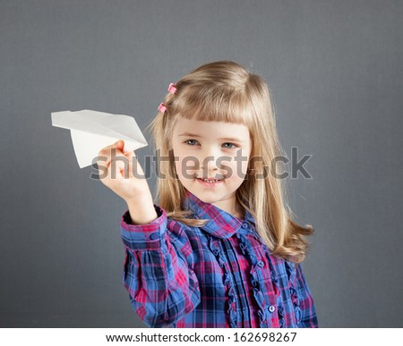 Smiling little girl flying paper plane on grey background