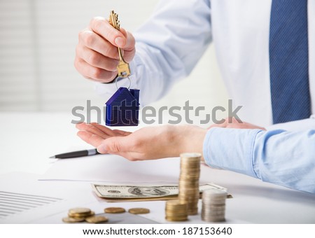 Real estate agent giving keys to the customer over the table with money and documents