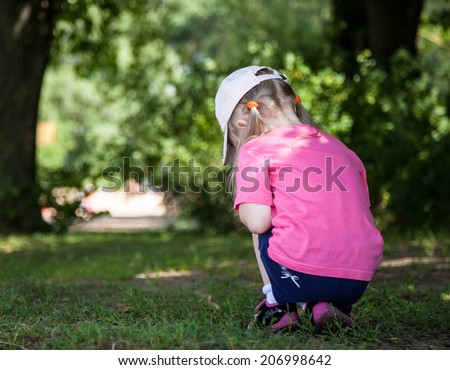 Little girl turning back and  gathering something in grass