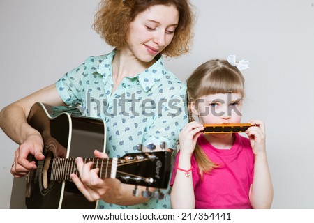 Yong mother and her  pretty daughter playing on  musical instruments, neutral background
