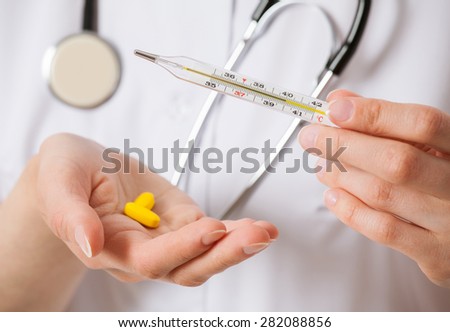 Doctor\'s hand holding thermometer and yellow tablets, closeup shot