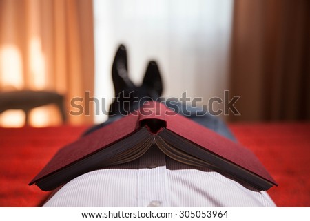 Relaxed gentleman lying on the bed with book with a red cover at home