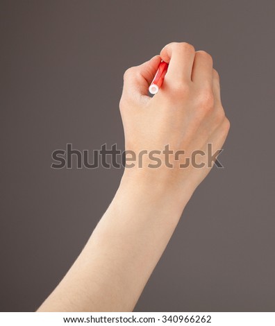 Female hand holding a red felt-tip pen on gray background
