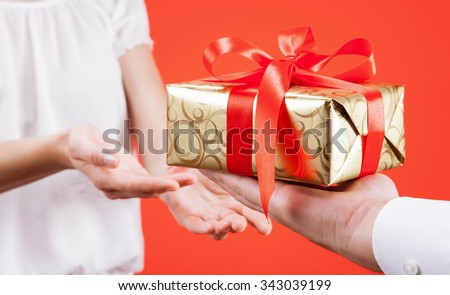 Man reaching out gift to young woman, red background