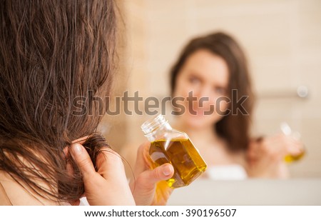 Smiling young woman applying oil mask to hair tips in front of a mirror; haircare concept