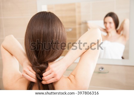 Young brunette plaiting her hair in front of a mirror in a bathroom