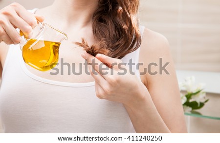 Unrecognizable woman applying oil mask to hair tips in a bathroom; beauty and haircare concept