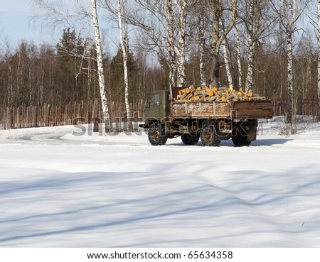 Truck transporting firewoods along the snow-covered road