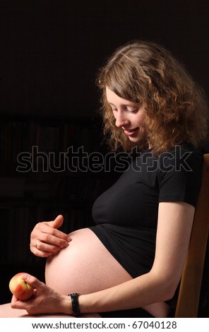 Smiling young pregnant woman with peach sitting on the chair
