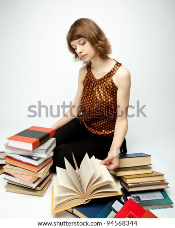 The beautiful young woman sitting among books and turning pages; neutral background