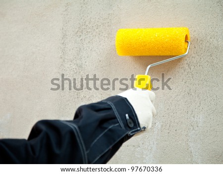 Working with paint roller; closeup of hand holding paint roller against the wall