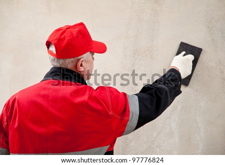 Back view of a plasterer in uniform working with float against the concrete wall