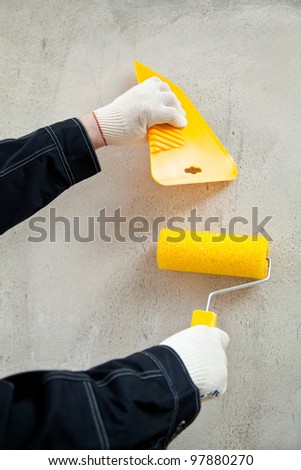 Painter with tools at workplace; hands of painter holding float and painting roller against the concrete wall