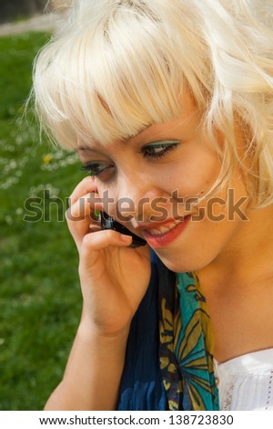 Portrait of young blond girl in a natural background, at the telephone