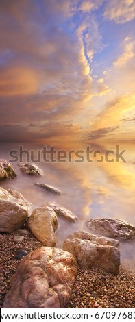 Sundown on sea with bright colour on the sky and stone on foregrounds. Vertical panorama