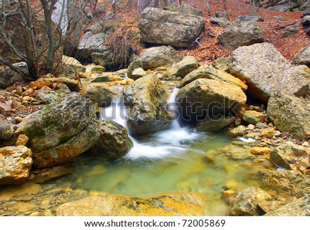 Waterfall and small lake amongst greater stone in wood. Natural composition
