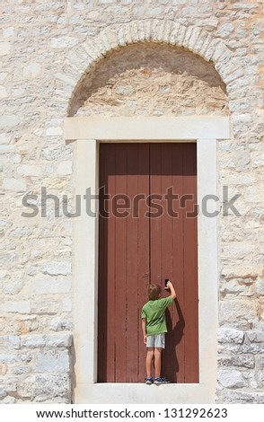 Curious young boy standing in front of an old big door of an ancient building