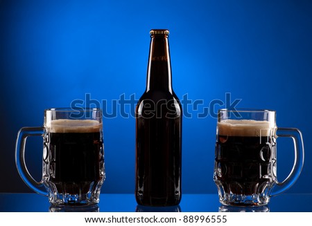 Brown beer bottle with two mugs on blue background