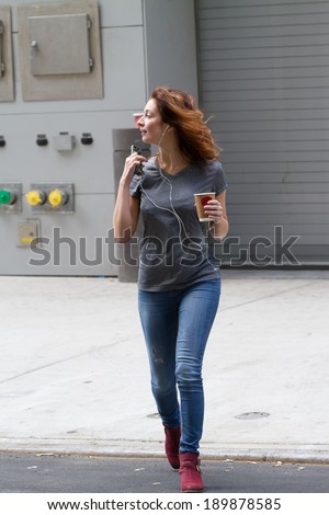 Sexy female crossing street, listening to music on smart phone with cup of coffee