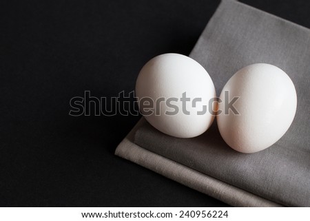 Close up two eggs on top of gray fabric and black surface with empty space for writing your own message